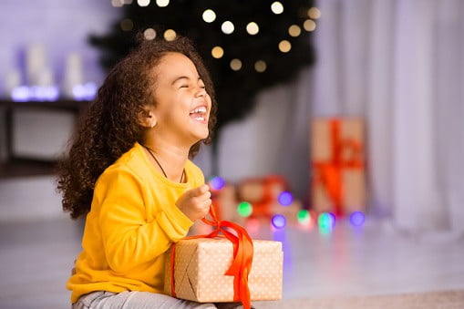 Excited african girl laughing with Christmas gift, empty space | Image: Unsplash