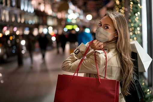 Happy woman Christmas shopping and wearing a facemask while carrying bags | Image: Unsplash