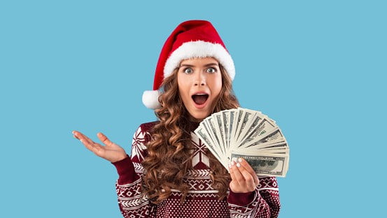 Shocked millennial girl in winter outfit holding fan of money on blue background | Image: Unsplash