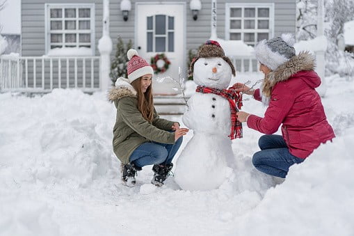 Mother and daughter making a snowman in front of the house | Image: Unsplash