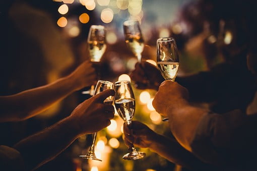 Numerous hands holding champagne flutes with champagne celebratory toast silhouettes | image: Unsplash