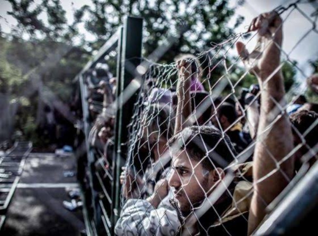 Migrants looking across a wire fence
