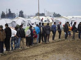 A group of migrants standing on a queue in a camp