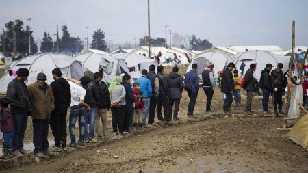 A group of migrants standing on a queue in a camp