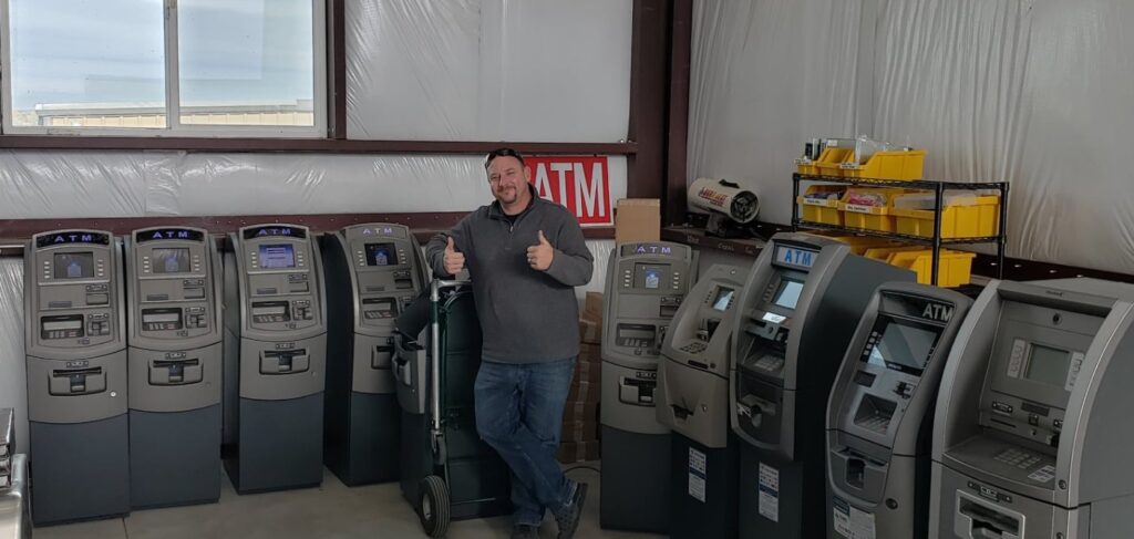 A man standing in a storage room with several ATMs