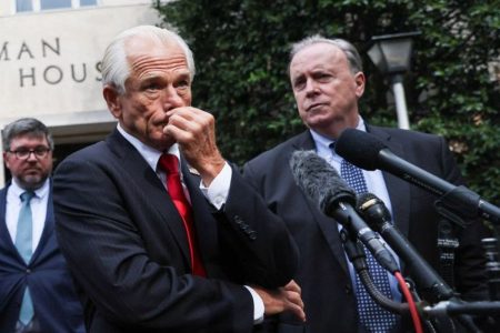 Trump's aide, Peter Navarro standing in front of a podium with hand on mouth