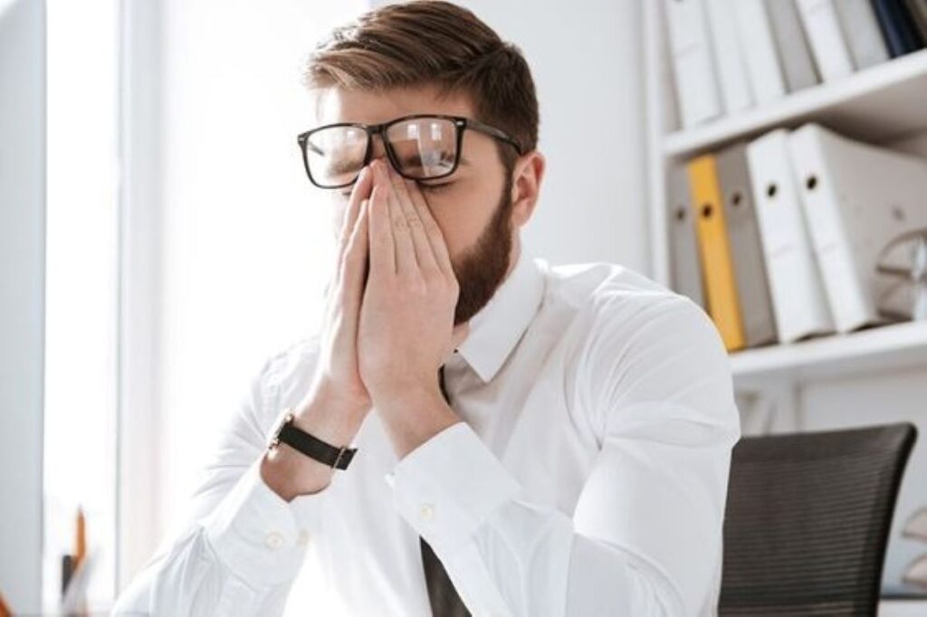 Stressful businessman in office touching eyes