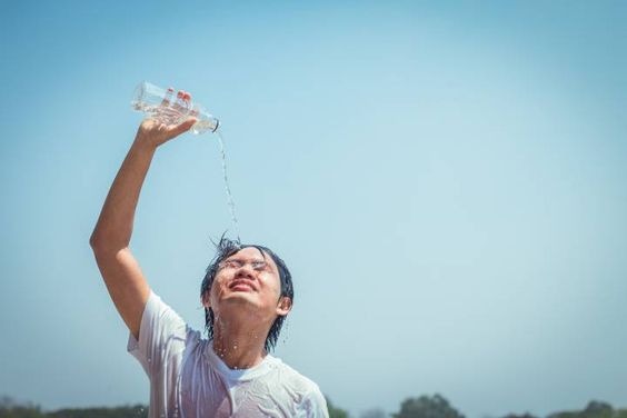 A boy standing outside pouring water from a bottle on himself