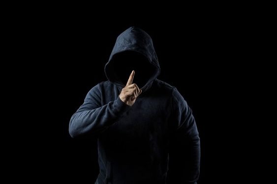 An anonymous man in a hoodie making the "be quiet" sign