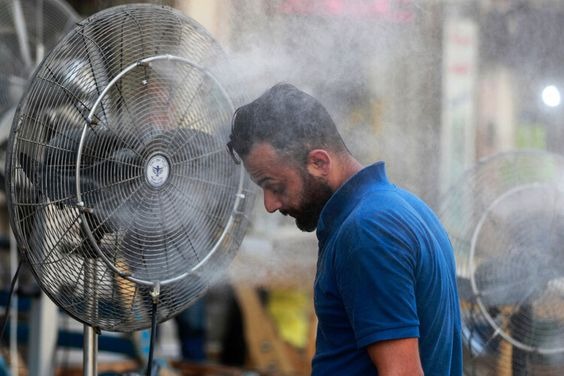 A man standing close to a fan to cool down