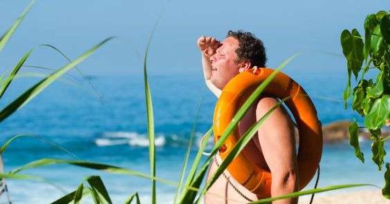 A man carrying a floater looking into the distance with the ocean in the background