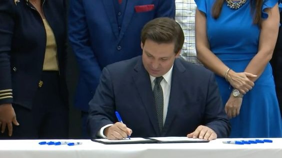 Ron DeSantis signing a document while surrounded by people