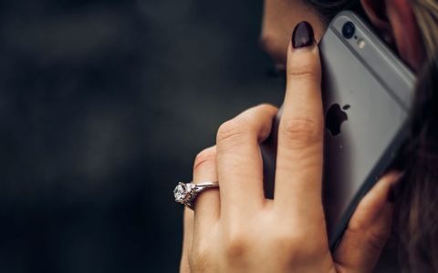 A woman with painted nails holding an iphone to her ear