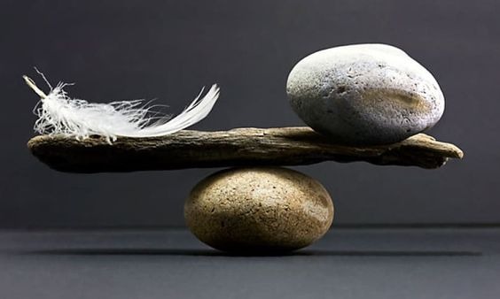 A feather and stone balanced on a piece of wood resting on a stone