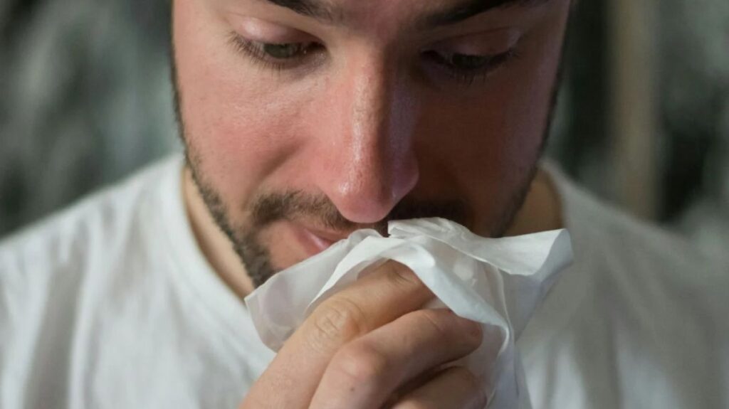 A close-up of a sick man with a white tissue.