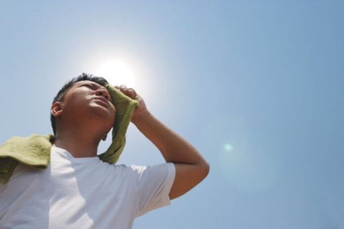 A man standing under a glaring sun wiping his forehead with a piece of clothing