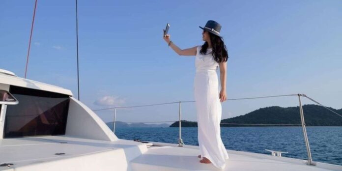 A woman in a long white gown taking a selfie on a yacht