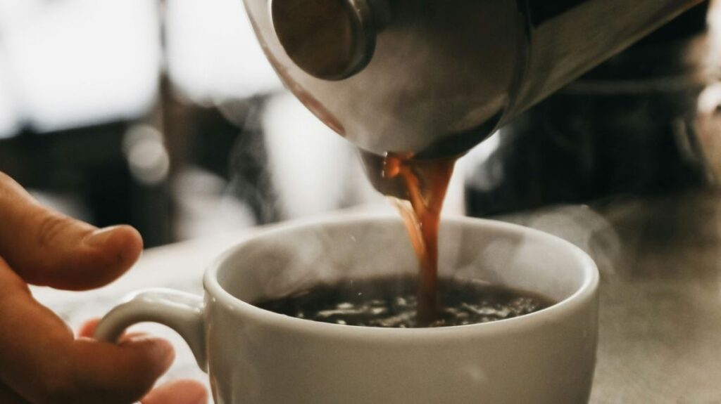 A person pouring hot coffee into a white mug.
